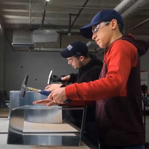 Two students hammering in a metalworking shop